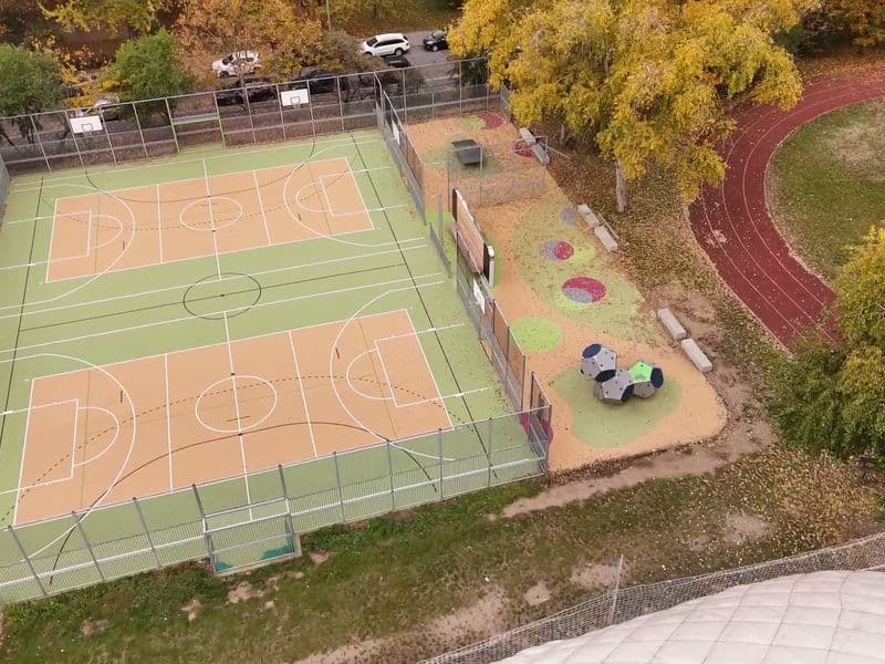 Nové multifunkční hřiště u školy z dronu: oplocené kurty, vedle hrací zóna, atletická dráha a podzimní stromy